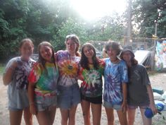 a group of young women standing next to each other in front of trees and tents