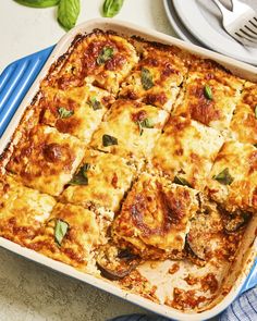 a casserole dish with meat, cheese and spinach on the side next to silverware