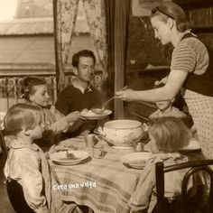 an old black and white photo of a woman serving food to children at a table