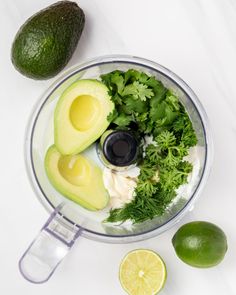 an avocado and cilantro in a blender next to limes