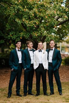 a group of men standing next to each other in front of a lush green tree