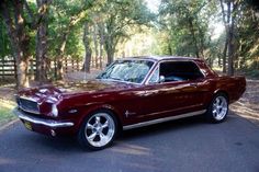 a maroon car is parked on the side of the road in front of some trees