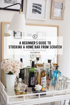 a white table topped with lots of bottles and flowers next to a mirror that says, a beginner's guide to stocking a home bar from scratch