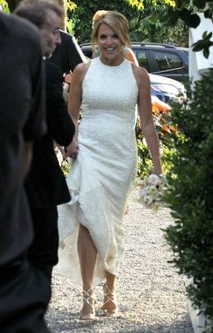 a woman in a white dress is walking down the street with another man behind her