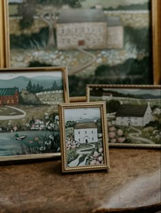 three framed pictures sitting on top of a wooden table next to each other with houses in the background