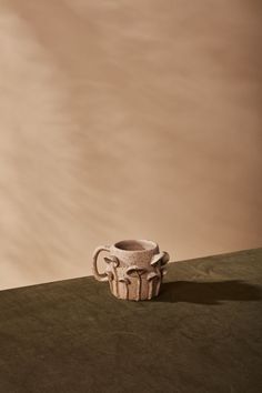 a small cup sitting on top of a table next to a wall with clouds in the background