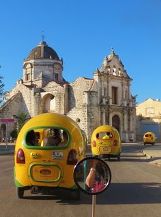 two yellow cars driving down the road in front of an old church