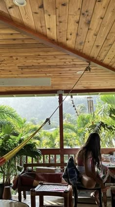 a woman sitting in a hammock on top of a wooden porch next to tables