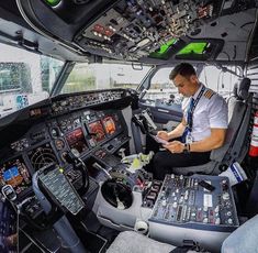 a man sitting in the cockpit of an airplane looking at his cell phone and other electronic equipment