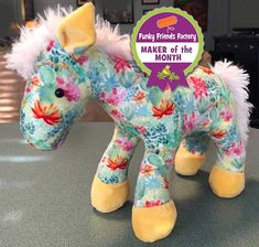 a stuffed toy horse sitting on top of a counter next to a sign that says maker of the month