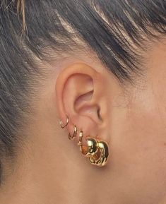 a close up of a person's ear with gold earrings on top of it