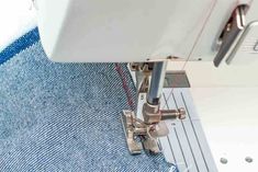 the sewing machine is working on some blue jeans with red stitchs and white thread