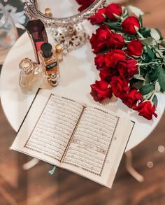 an open book sitting on top of a table next to red roses and a mirror