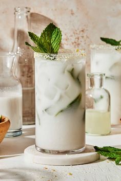 a glass filled with ice and mint sitting on top of a table next to other drinks