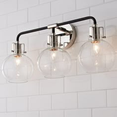 three clear glass globe lights hanging from a metal fixture on a white brick wall in a bathroom