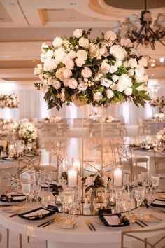 a tall centerpiece with white flowers and greenery sits on top of a round table