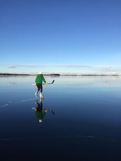 a man in green shirt and white hat on water holding a hockey stick with reflection