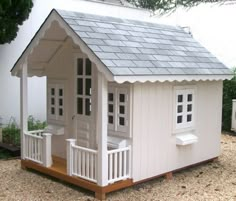 a small white house with a porch and windows on the roof is sitting in gravel