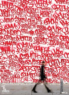 a man walking past a wall covered in red grafitti letters and graffiti on it