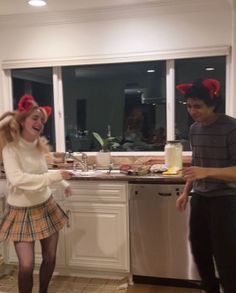 a man and woman standing in a kitchen next to each other with red bows on their head