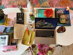 an open laptop computer sitting on top of a white table covered in books and other items