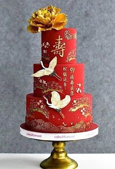 a three tiered red cake with gold decorations on top and flowers in the middle