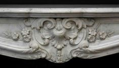 an ornate white marble fireplace mantel with flowers and leaves on the top, set against a black background