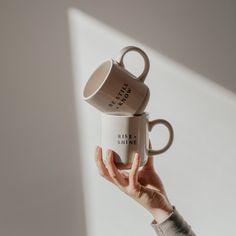 a woman holding two coffee mugs in her hand with the words rise and shine on them