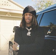 a man with dreadlocks standing in front of a car