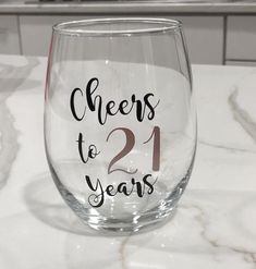 a wine glass with cheers to 21 years written on it sitting on a counter top