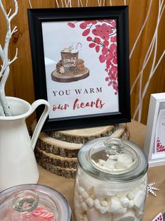 a table topped with jars filled with marshmallows next to a sign that reads, you warm our hearts