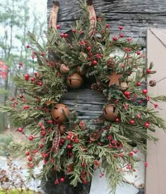 a christmas wreath hanging on the side of a building with red berries and pine cones