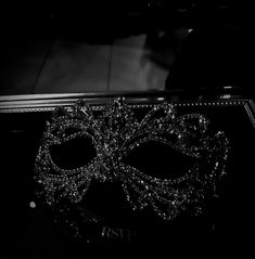 a black and white photo of a masquerade mask on a mirrored table top