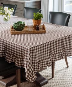 a dining room table covered with a checkered tablecloth and potted plants on it