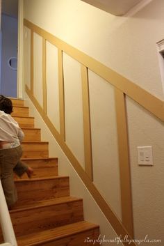 a young child climbing up the stairs in a house with white walls and wood handrails