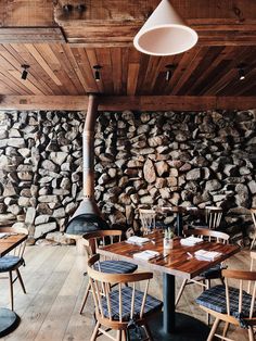 a restaurant with wooden tables and chairs next to a wall of stacked wood planks