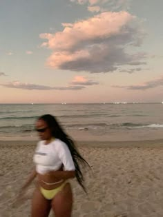 a woman is running on the beach with her frisbee in front of her