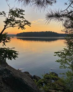 the sun is setting over a lake with rocks and trees