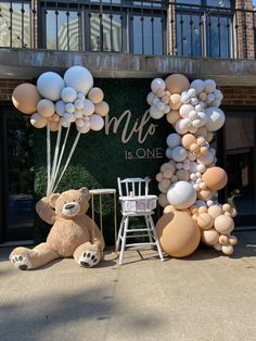 a teddy bear sitting in front of a balloon arch