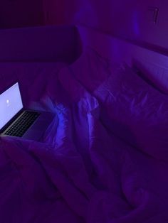 an open laptop computer sitting on top of a purple bed in a room with white walls