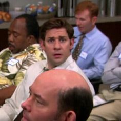 a group of men sitting next to each other in front of a tv screen with one man looking at the camera