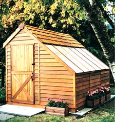 a small wooden shed sitting in the middle of a yard next to some flowers and trees