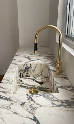 a bathroom sink with a gold faucet and marble counter top next to a window