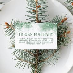 a white plate topped with a green and white book for baby label next to pine branches