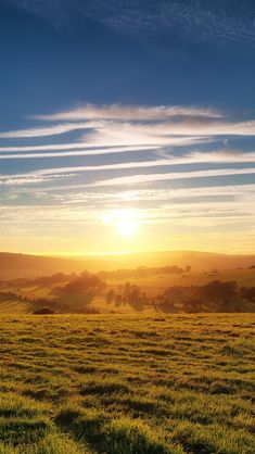 the sun is setting over an open field with green grass and hills in the distance