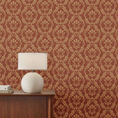 a lamp sitting on top of a wooden table next to a wallpapered wall