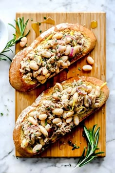 two pieces of bread with white beans and herbs on top, sitting on a cutting board