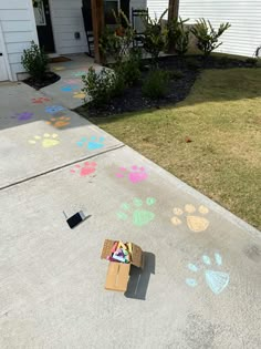 the sidewalk is covered in chalk and has paw prints painted on it, along with a cardboard box full of crayons