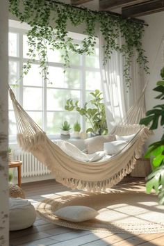 a white hammock hanging from the ceiling in front of a window with potted plants