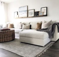 a living room with white couches and pictures on the wall above them, along with a round wicker coffee table